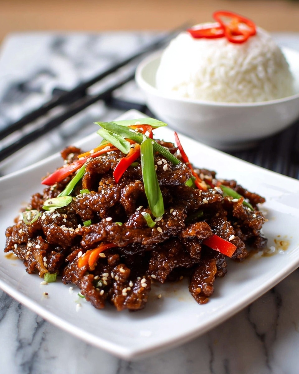 A white square plate holds a mound of crispy, glossy fried beef strips covered in a dark brown sticky sauce mixed with thin orange carrot strips and small bright red chili slices, sprinkled with white sesame seeds. On top, layers of fresh sliced green scallions add a bright contrast. In the background, a white bowl filled with fluffy white rice is topped with two chili slices, sitting on a white marbled surface with black chopsticks placed beside it. Photo taken with an iphone --ar 4:5 --v 7