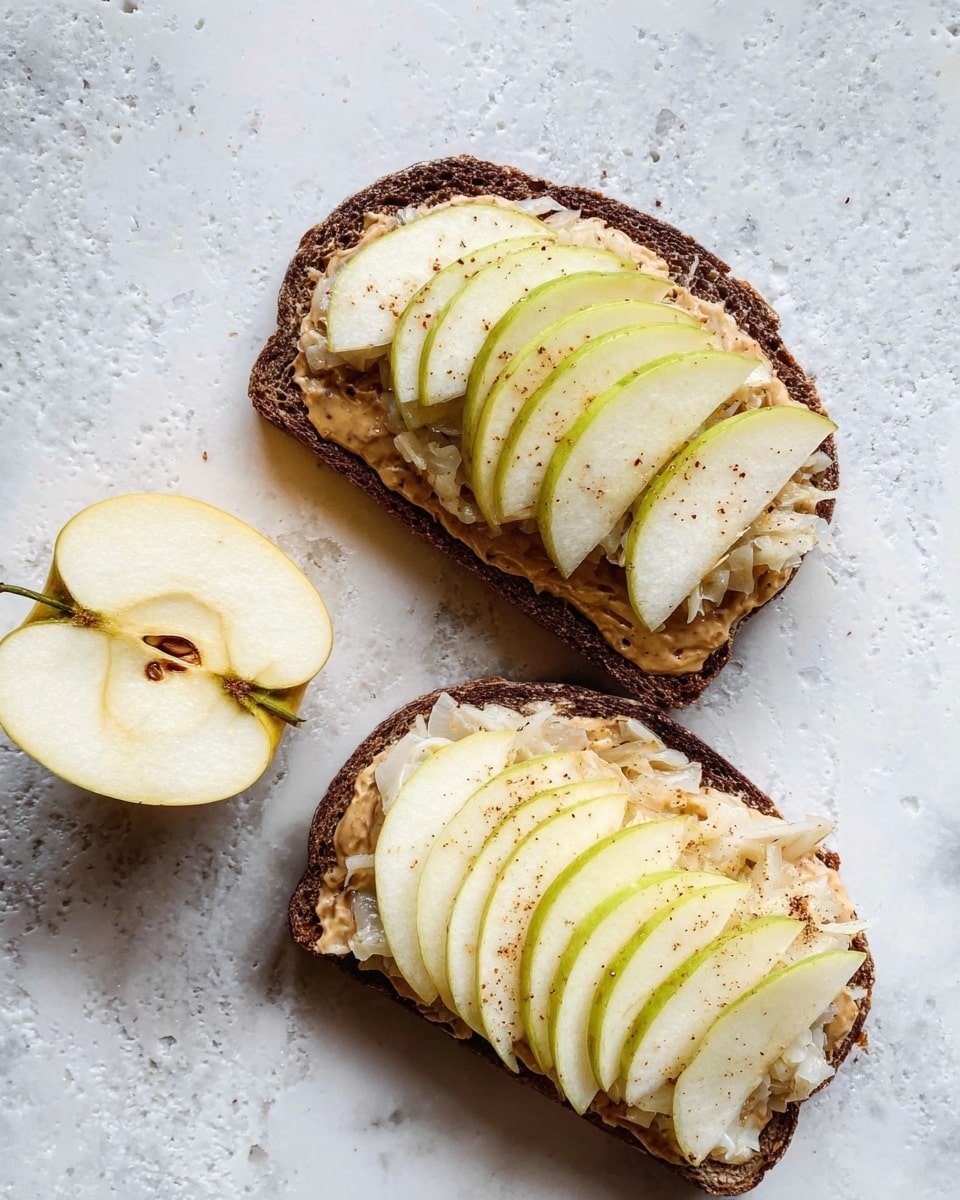 The image shows two slices of dark toasted bread on a white marbled surface, topped with layers of light brown spread, a fluffy layer of sauerkraut with a slightly wet texture, and neatly arranged thin slices of pale yellow apple with a hint of green skin on top. One half apple sits near the bread slices on the surface, with the fruit's pale yellow interior visible. The colors range from dark brown of the toast to soft creamy and natural fruit tones, creating a fresh and simple look. Photo taken with an iphone --ar 4:5 --v 7