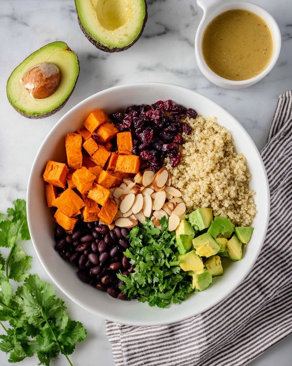 A bowl filled with a colorful quinoa salad showing about four layers: the bottom layer is light beige cooked quinoa, mixed with bright orange roasted sweet potato cubes, black beans, and small avocado chunks. The top layer has scattered almond slices, dark red dried cranberries, and chopped green cilantro sprinkled on top. A lime wedge rests on the edge of the bowl, which is white, and two silver spoons are placed inside. The bowl sits on a white marbled surface with loose cilantro leaves, half a lime, a small glass bowl of dried cranberries, and a striped cloth cloth around it. Photo taken with an iphone --ar 4:5 --v 7