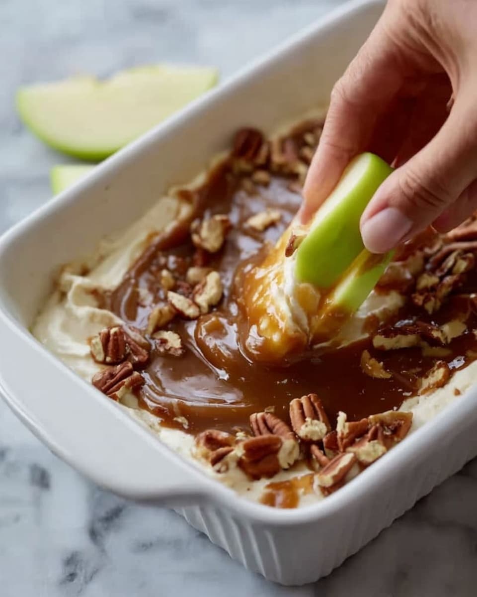 A white rectangular dish filled with a creamy layered dessert, showing two clear layers: a thick, smooth, white base and a shiny caramel brown topping sprinkled with pecan pieces. A spoon scoops into the dessert, lifting a mix of the creamy white layer with caramel swirls and nuts, while the edges reveal some layering. On the white marbled surface around the dish, there are red and green apple slices. Photo taken with an iphone --ar 4:5 --v 7