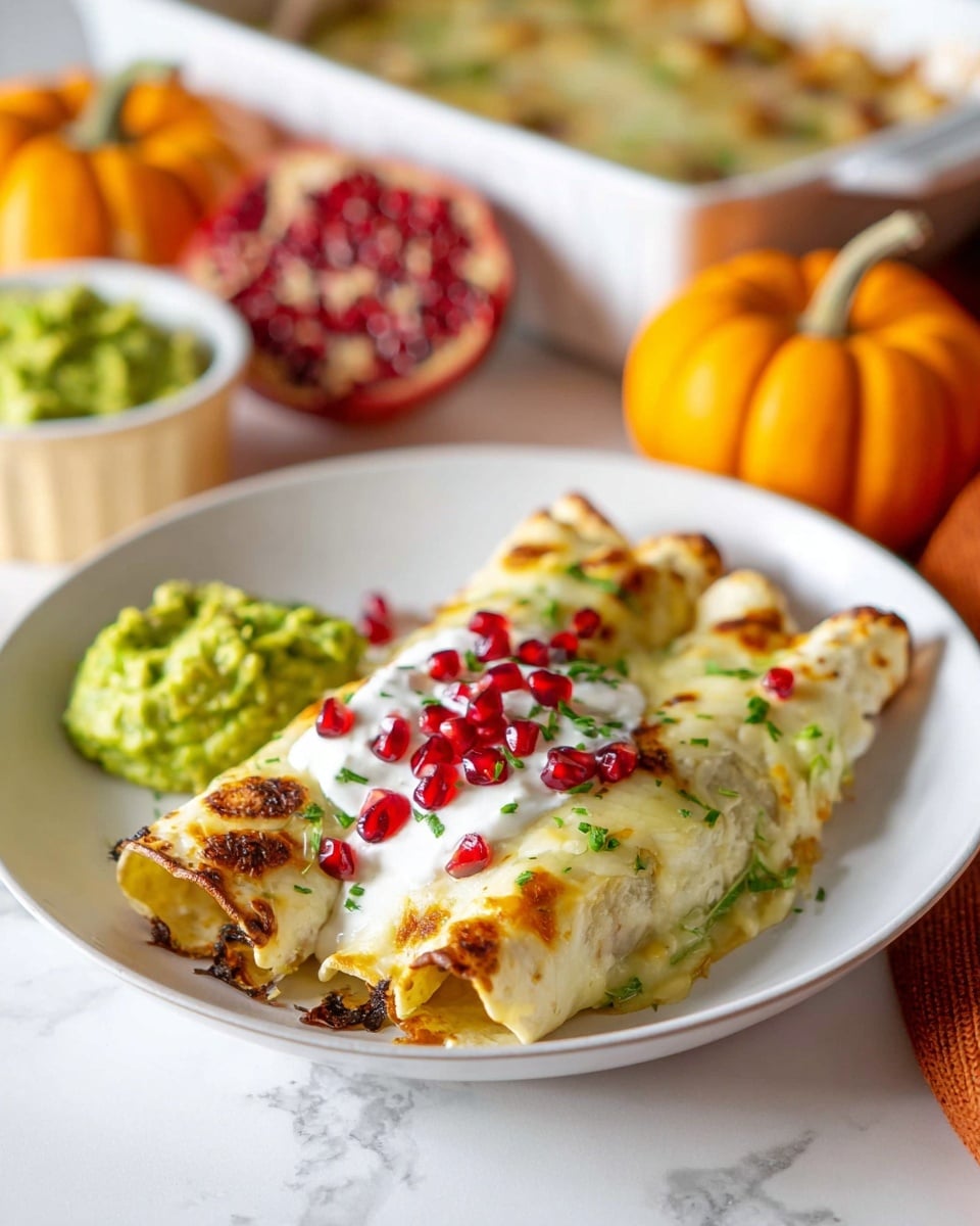 A white rectangular baking dish holds multiple rolled enchiladas arranged in one layer, each covered in melted light yellow cheese with parts browned from baking, topped with white sour cream drizzles and sprinkled with finely chopped green herbs. The enchiladas themselves show a dark brown tortilla base peeking through the cheese and sauce. The dish sits on a colorful autumn-themed cloth with a pattern of leaves. In the blurred background, there are two small pumpkins, one white with yellow stripes and one orange, alongside a bowl of green guacamole topped with red pomegranate seeds, all set against a white marbled surface. Photo taken with an iphone --ar 4:5 --v 7