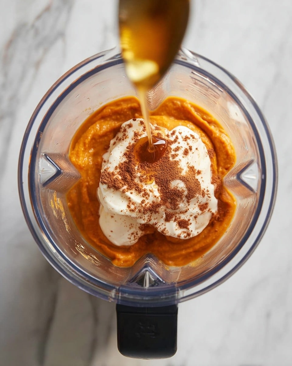 A close-up image of a white bowl filled with three distinct layers: the bottom layer is a smooth, thick orange smoothie that fills most of the bowl; on one side, a cluster of crunchy granola with a light brown color covers about one-third of the bowl’s edge; the top of the orange smoothie is swirled gently with a dusting of cinnamon and thick, glossy honey drizzled in a curve over one part of the swirl. The bowl sits on a white marbled surface, with a shiny gold spoon placed beside it. photo taken with an iphone --ar 4:5 --v 7