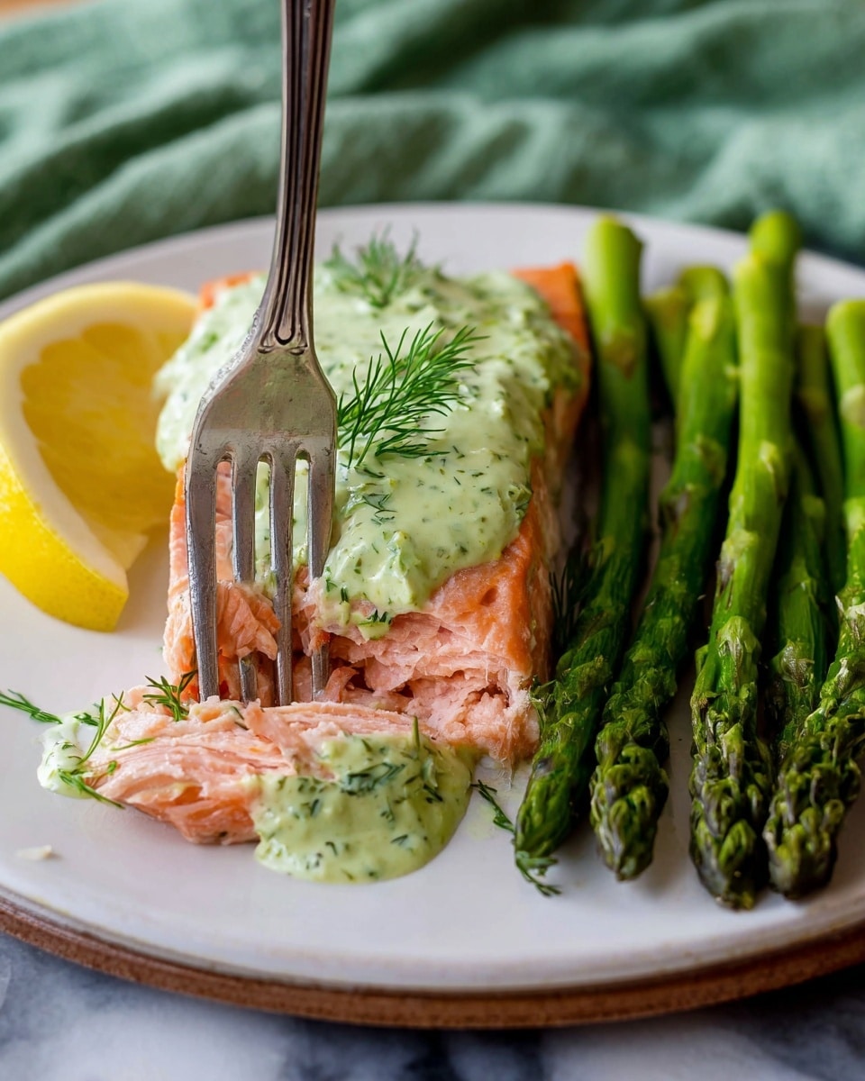 A thick, light pink cooked salmon fillet forms the base layer on a white plate with embossed edges. The second layer is a creamy, pale green sauce with herb specks, spread evenly over the salmon. On top, there are two lemon slices, one upright near the center and a second partially visible behind it, each garnished with sprigs of fresh green dill. Surrounding the salmon are bright green roasted asparagus stalks arranged around the edge of the plate in an uneven circle. The plate is set on a white marbled surface. photo taken with an iphone --ar 4:5 --v 7