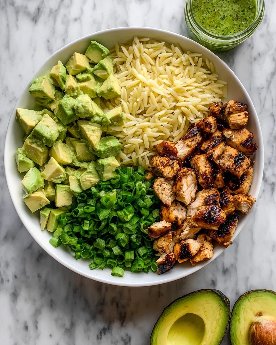 A large white bowl filled with a layered dish starting with a base of small, rice-shaped orzo pasta in a light yellow-green color mixed evenly with finely chopped green herbs. On top, there are medium-sized pieces of grilled chicken with a golden-brown, slightly charred texture. Alongside the chicken are chunks of vibrant green avocado with a smooth texture, scattered throughout the bowl. The dish is garnished with chopped green onions and fresh parsley leaves, creating a mix of light and dark green shades that contrast with the pale orzo and cooked chicken. Two gold spoons rest inside the bowl on opposite sides. The bowl sits on a white marbled surface, with two halves of fresh avocado nearby and a small bowl of green dressing in the top right corner. Photo taken with an iphone --ar 4:5 --v 7