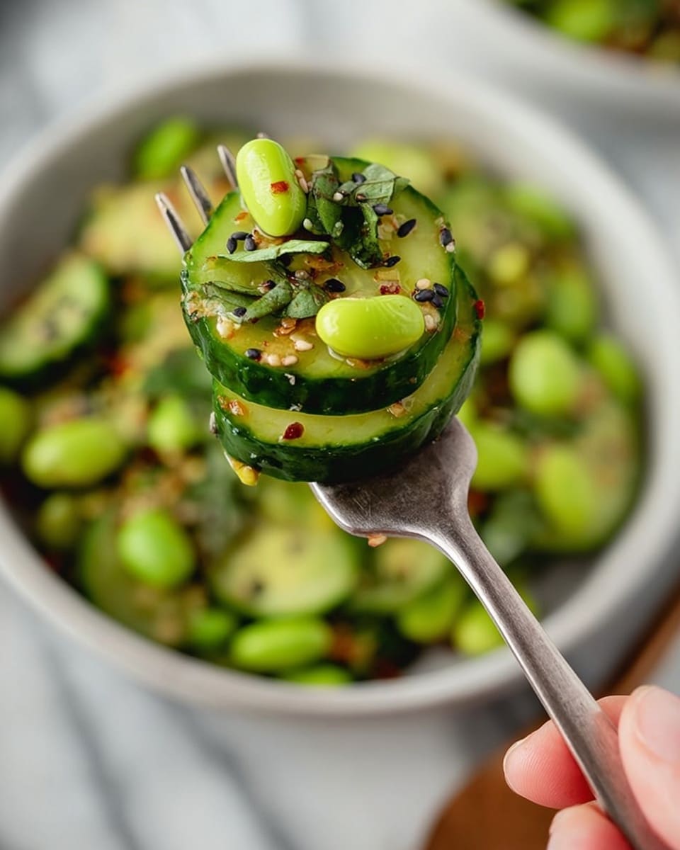 A bowl filled with multiple round slices of cooked zucchini, showing light green centers and darker green skin edges, mixed with bright green edamame beans scattered throughout. There are small bits of green herbs and chopped green onions spread evenly over the zucchini slices. White and black sesame seeds are sprinkled on top along with tiny bits of red chili flakes. A small white bowl with red chili oil and flakes is placed nearby on a white marbled surface, with a pair of chopsticks featuring brown tops and black tips resting beside the bowl. A purple cloth is placed beside the bowl. Photo taken with an iphone --ar 4:5 --v 7