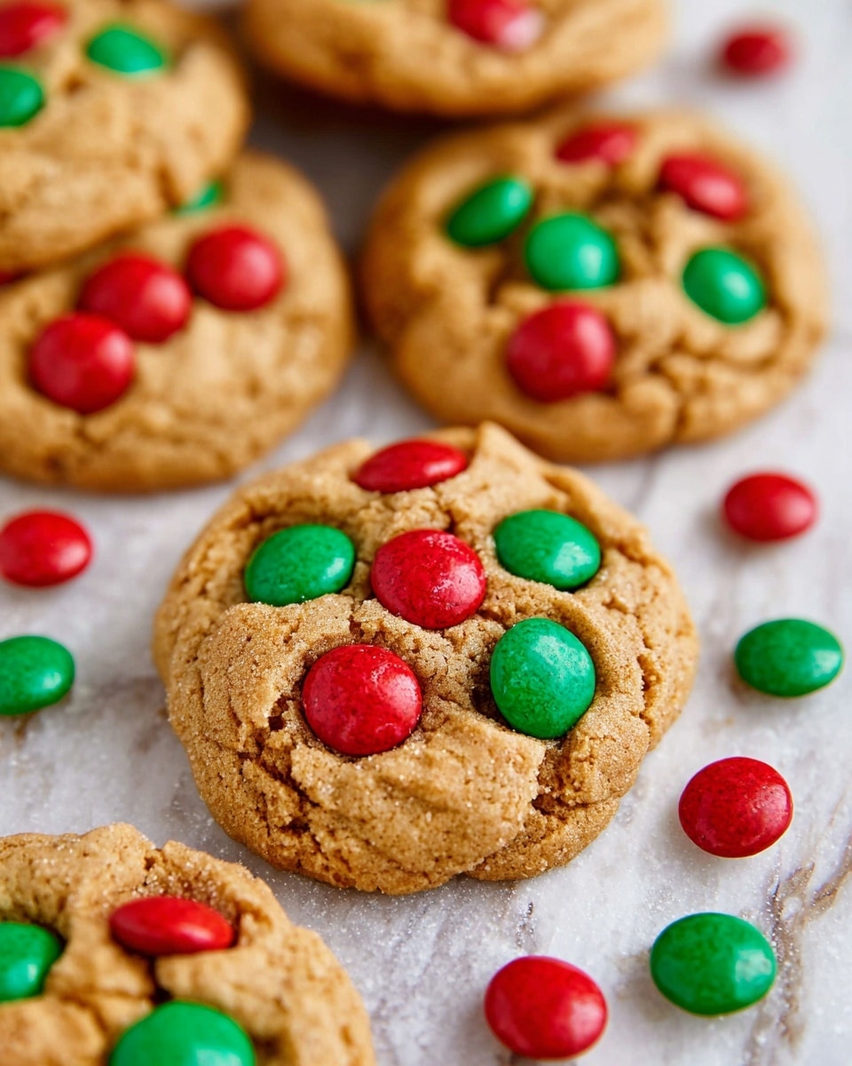 The image shows several round cookies with a soft, slightly cracked light brown surface, each embedded with bright red and green candy-coated chocolates scattered across the top. The cookies are placed directly on a white marbled surface, giving a clean and fresh look. The texture of the cookies is chewy with visible creases and small cracks. Additional red and green candies are scattered around the cookies on the surface, creating a festive and colorful scene. photo taken with an iphone --ar 4:5 --v 7