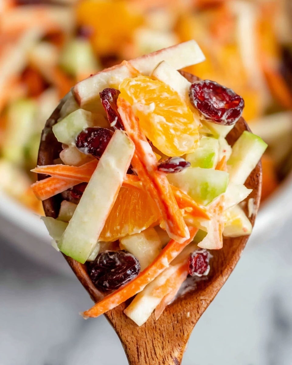 A clear glass bowl filled with a colorful salad sitting on a white marbled surface. The salad has many layers: bright orange mandarin pieces scattered throughout, thin white apple slices with smooth edges, crunchy green apple strips, shredded orange carrots, and dark red dried cranberries. All ingredients are mixed together giving the salad a fresh, textured look. Around the bowl, there is a gray cloth with a herringbone pattern and two wooden spoons placed below it. photo taken with an iphone --ar 4:5 --v 7