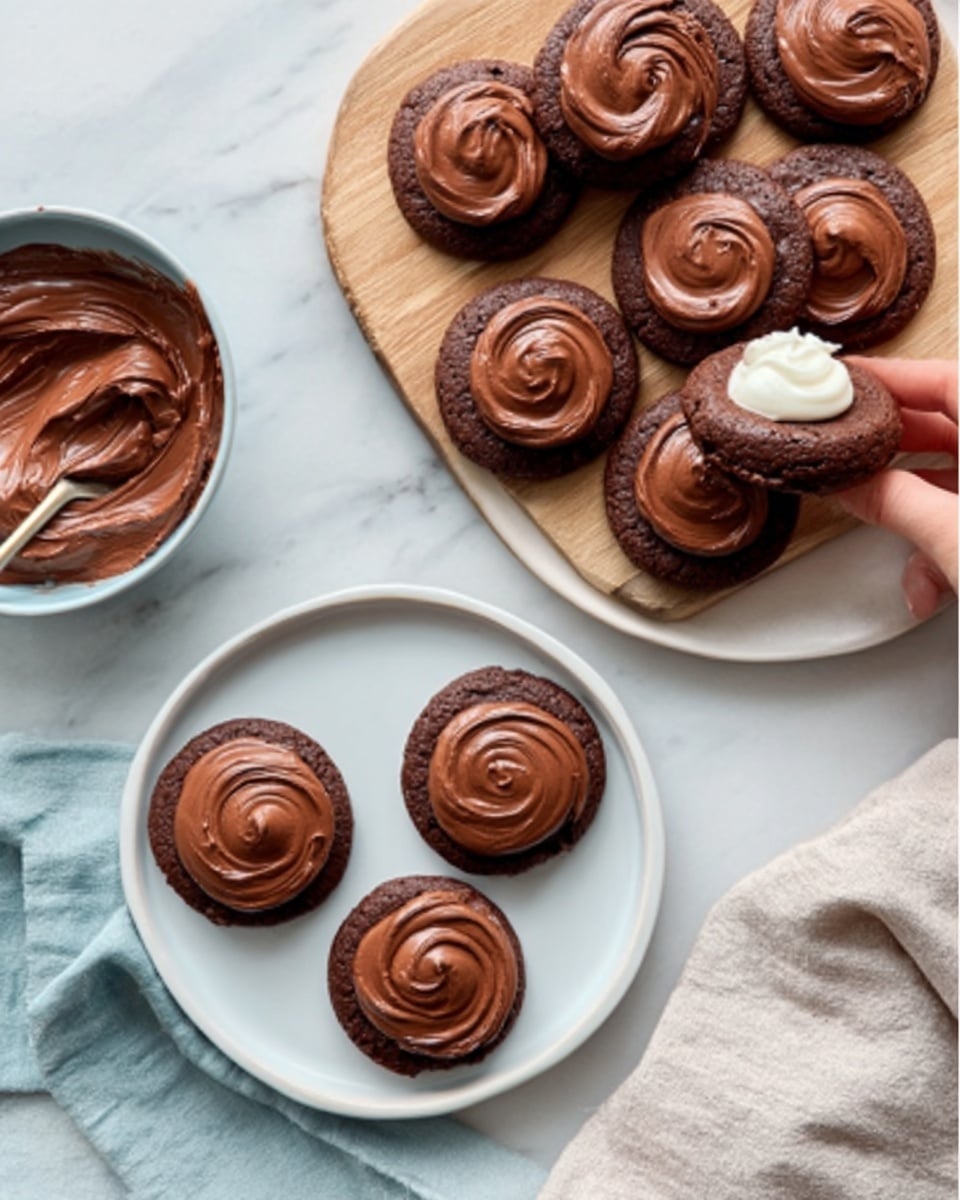 The image shows a white plate on the right filled with round chocolate cookies topped with smooth swirls of chocolate frosting, rich and glossy in texture. On the lower left, there is another white plate with three similar cookies, each with thick, creamy, shiny chocolate frosting swirled on top. A woman's hand is spreading frosting on a cookie next to a small bowl filled with more chocolate frosting in the top left. The cookies have a dark brown color and slightly rough texture, while the frosting is smooth and shiny. The scene is set on a white marbled surface with a soft-colored cloth napkin at the bottom right. Photo taken with an iphone --ar 4:5 --v 7