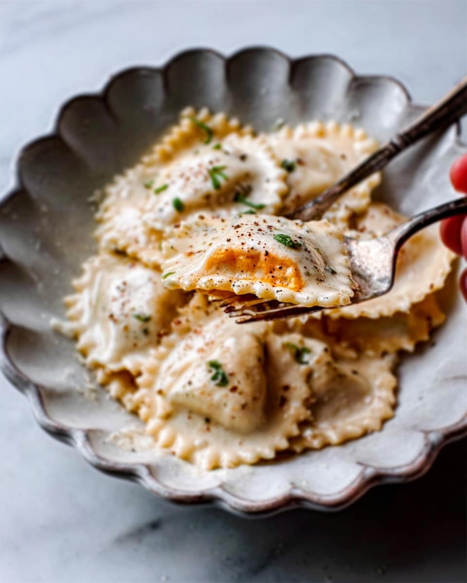 The image shows a close-up of a white, scalloped-edged plate filled with ravioli covered in a creamy white sauce. The ravioli are light beige with visible herbs and tiny black pepper specks on top. One ravioli is held by a woman's hand, showing a bright orange filling inside, creating a contrast with the pale pasta and sauce. The plate rests on a white marbled surface, adding a clean and elegant look. A fork and knife lie on the plate’s edge, with soft natural lighting enhancing the creamy textures and smooth edges of the pasta. Photo taken with an iphone --ar 4:5 --v 7