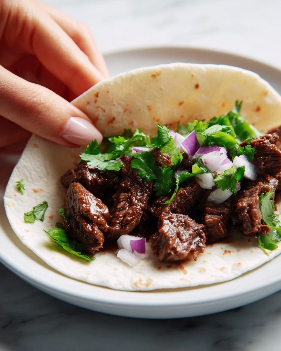 A close-up of a soft, white tortilla held by a woman's hand, filled with several pieces of dark brown, cooked beef with a tender, juicy texture. On top, there are small, chopped pieces of purple and white onion mixed with fresh, bright green cilantro leaves, adding a fresh color contrast. The tortilla is being gently folded while resting on a simple white plate, all placed on a white marbled surface. photo taken with an iphone --ar 4:5 --v 7