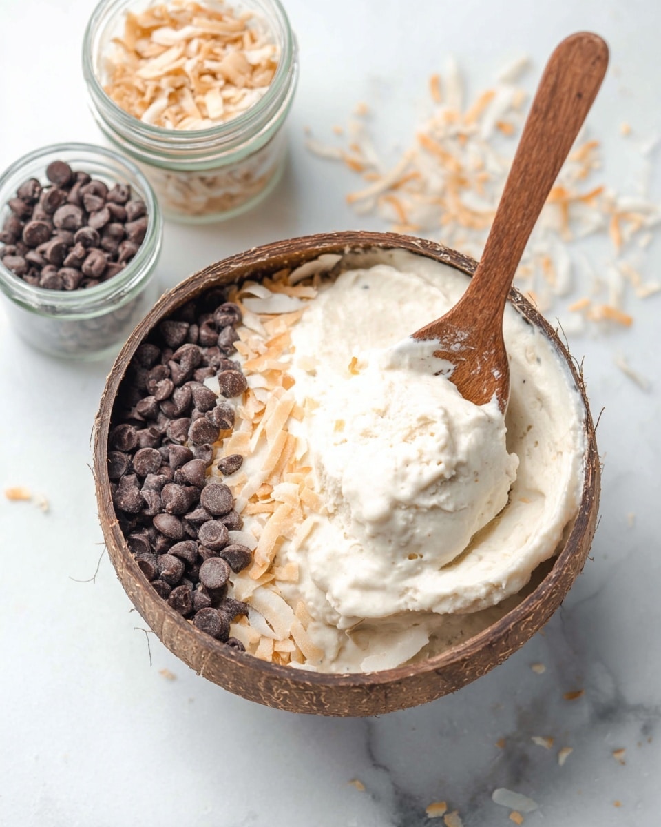 A round brown bowl is filled with a creamy off-white smooth mixture that makes up the main layer. On top, there are two topping sections that cover about half of the surface: one side has golden toasted shredded coconut, and the other side has small dark brown chocolate chips, with a line of chocolate chips between the coconut and the plain mixture. The bowl is set on a white marbled surface with scattered chocolate chips and shredded coconut nearby. A wooden spoon lies to the right of the bowl. In the background, there are two small clear glass bowls, one filled with shredded coconut and the other with chocolate chips. Photo taken with an iphone --ar 4:5 --v 7