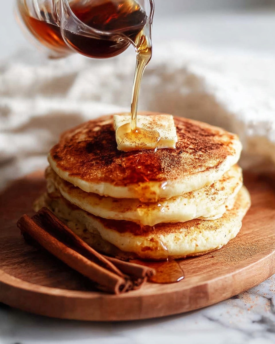 A stack of four golden-brown pancakes sits in the center of a white plate, each layer slightly fluffy and thick. The top pancake is drizzled with honey or syrup that glistens under the light, and it is topped with mixed berries including red raspberries, blue blueberries, and a small green mint leaf. More berries surround the stack on the plate, adding splashes of red and blue color against the white surface. The scene is set on a white marbled table, with a blurred white bowl of blueberries in the background and scattered mint leaves and berries around the plate. Photo taken with an iphone --ar 4:5 --v 7