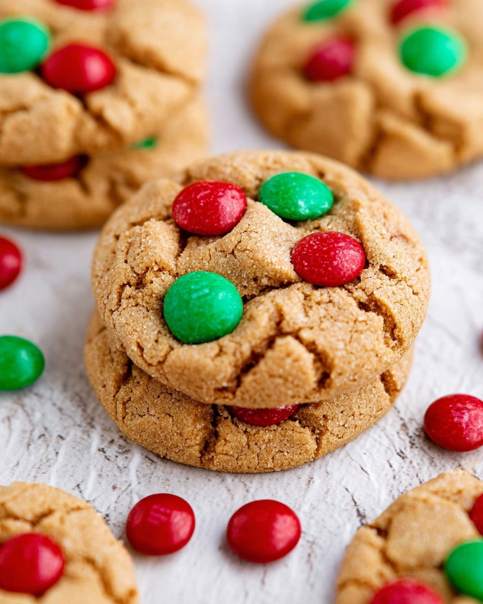 The image shows a close-up of round cookies with a light brown, slightly cracked texture. Each cookie is decorated with red and green candy-coated chocolate pieces embedded on the top surface. The cookies are stacked and spread out on a white marbled surface, with some loose red and green candies scattered around. The cookies appear soft and thick, with a rough, crumbly texture. Photo taken with an iphone --ar 4:5 --v 7