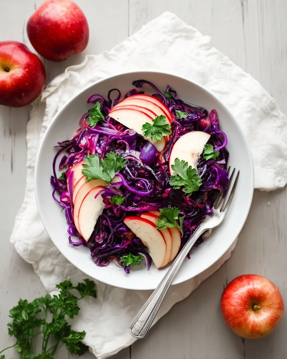 A white bowl holds a colorful salad featuring thin spiralized strands of deep purple cabbage at the base, mixed with crisp, thin slices of red apple with white flesh, arranged evenly throughout the cabbage. Bright green parsley leaves are scattered on top and around the salad, adding fresh bursts of color and texture. The salad sits on a white cloth over a white marbled surface, with a silver fork resting on the bowl’s edge. Around the bowl, there are whole and halved red apples and additional parsley sprigs, enhancing the natural and fresh look. photo taken with an iphone --ar 4:5 --v 7