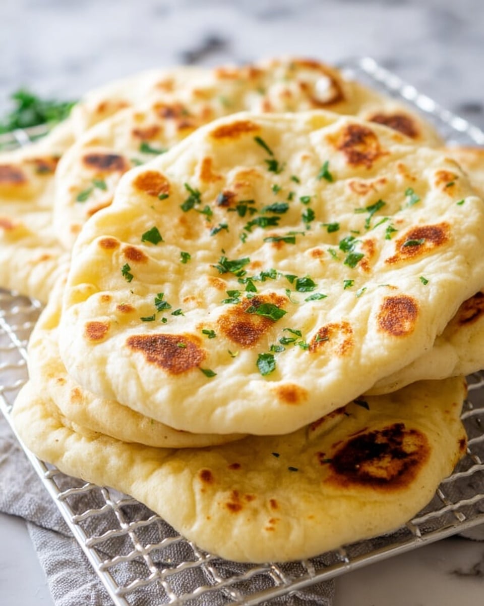 The image shows a stack of flatbreads with a golden-brown toasted surface and soft, slightly puffy texture, sprinkled with small green herb pieces on top. Each flatbread layer has uneven bubbles and browned spots, indicating it was cooked on high heat. The flatbreads are piled casually on a white wire cooling rack, placed over a white marbled surface that adds a clean background detail. Photo taken with an iphone --ar 4:5 --v 7