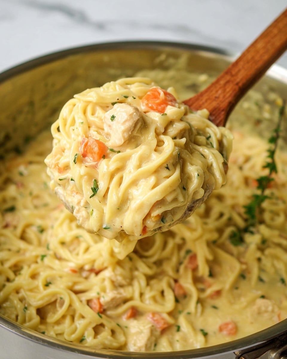 The image shows a white bowl filled with a creamy noodle soup. The top layer is a light yellow creamy broth with soft noodles mixed in. Within the broth, there are visible chunks of carrot slices in orange, small pieces of white tofu or chicken, and some herbs sprinkled lightly on top. The bowl sits on a blue and white striped cloth on a white marbled surface, with a metal spoon resting beside it on the right. A sprig of fresh green rosemary lies in front of the bowl, and in the background, there are two white jars with purple flower designs. photo taken with an iphone --ar 4:5 --v 7