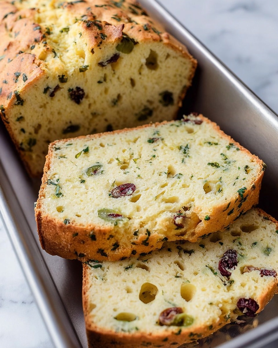 A close-up image shows a loaf of savory bread with three visible layers: the top crust is golden brown with a rough texture and sprinkled with dried herbs and small black olive pieces; the middle slice layer reveals a soft, light yellow interior with dark green olive bits and small chunks of red and black olives distributed evenly; the bottom slice layer shows the same soft texture and olive pieces, with the crust slightly browned around the edges. The bread is placed on a round white plate, all set on a white marbled surface. photo taken with an iphone --ar 4:5 --v 7