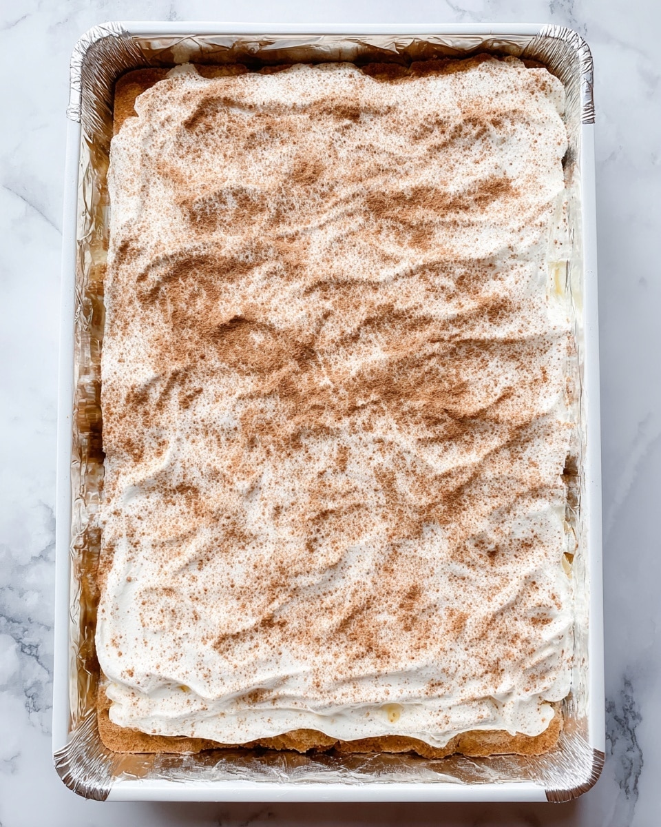 A close-up image of a stacked layered dessert with six visible layers. Each layer alternates between golden-brown crispy crackers and smooth, creamy white filling, with a sticky golden caramel layer near the top. The top layer is sprinkled with a mix of light brown cinnamon and sugar, giving it a grainy texture. Crumbs and broken pieces are scattered around on a white marbled surface underneath the stack, and blurry pieces of the dessert are in the background. photo taken with an iphone --ar 4:5 --v 7