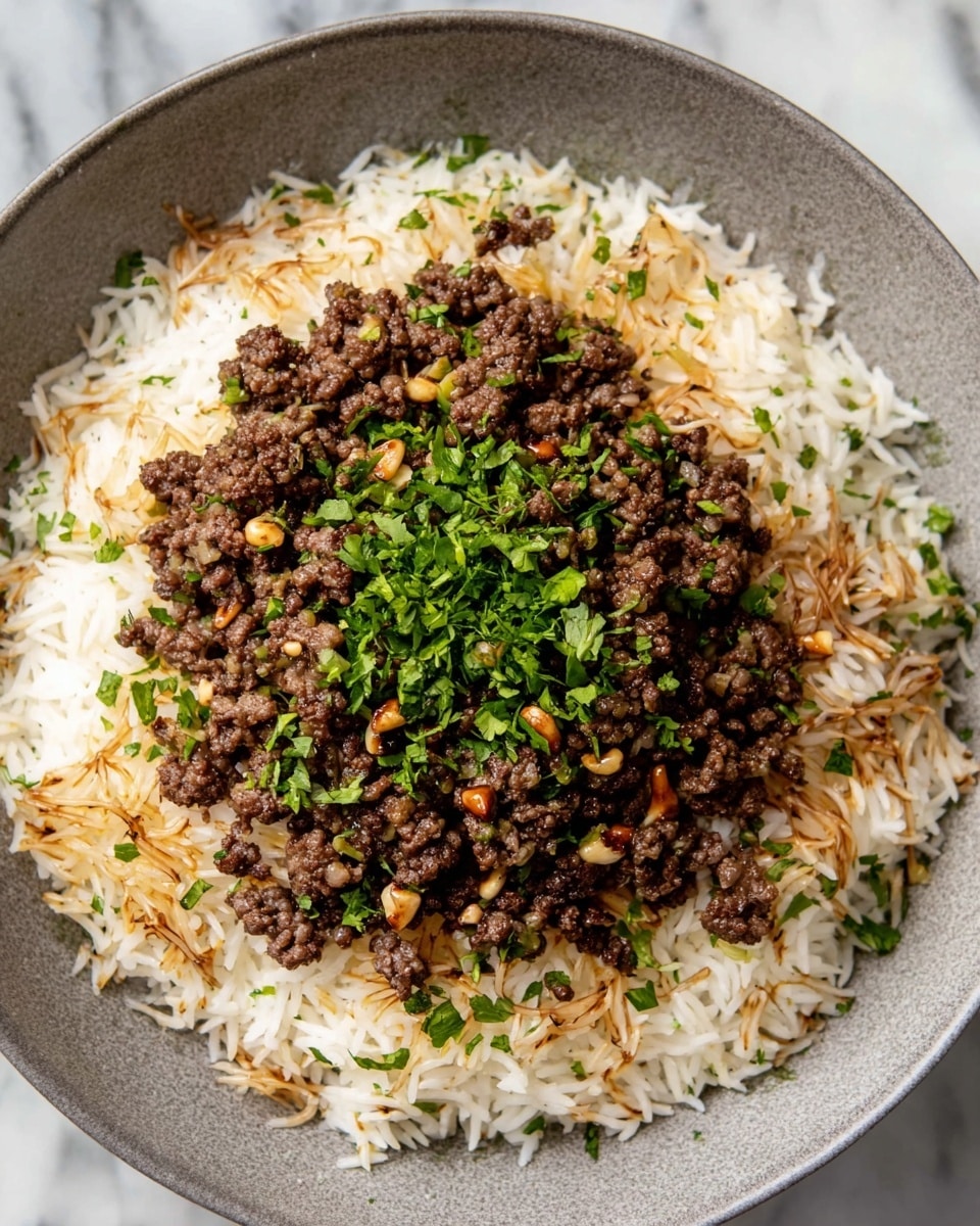 A grey bowl filled with two main layers: the bottom layer is a generous serving of white rice mixed with toasted brown vermicelli noodles, creating a mixed texture of soft grains and crunchy noodles around the edges, sprinkled lightly with chopped green herbs. The top layer is a mound of finely ground cooked beef mixed with small pieces of onions and pine nuts, dark brown and juicy with a slightly oily sheen, also garnished with fresh chopped green herbs, all positioned neatly in the center on top of the rice. The bowl sits on a surface with a white marbled texture. photo taken with an iphone --ar 4:5 --v 7