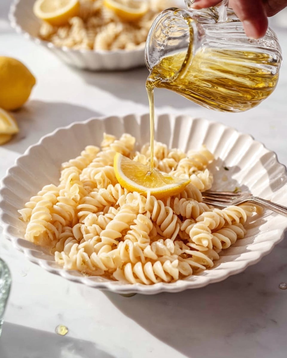 A white scalloped bowl is filled with a single layer of rotini pasta coated in a creamy, light beige sauce with visible black pepper specks, giving the pasta a slightly textured appearance; a fork rests inside the bowl on the right side, partially under the pasta. Around the bowl, on a white marbled surface, are two lemon wedges in the upper left corner, scattered small green basil leaves and chopped nuts on the lower left side, and parts of two more bowls with the same pasta visible near the edges, creating a bright, fresh setting. photo taken with an iphone --ar 4:5 --v 7