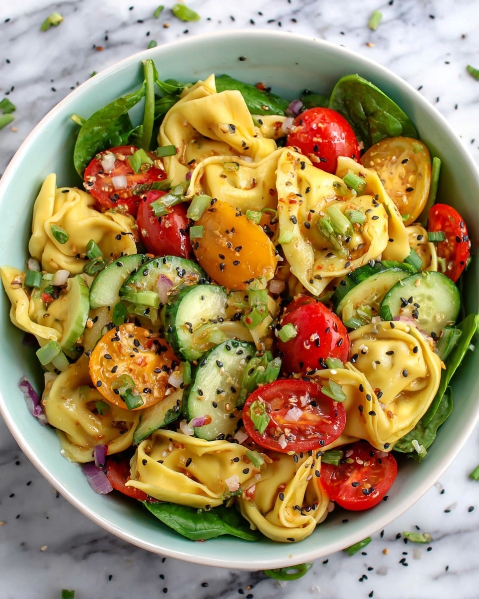 A white bowl filled with a colorful salad showing three main layers: the bottom layer has fresh green spinach leaves, the middle layer features yellow tortellini pasta with a smooth and soft texture, and the top layer includes sliced green cucumbers, halved red and yellow cherry tomatoes, and small green onion pieces. The salad is sprinkled with black sesame seeds and dressed with a glossy sauce, making the ingredients shine. The bowl sits on a white marbled surface with a few scattered black sesame seeds around. Photo taken with an iphone --ar 4:5 --v 7