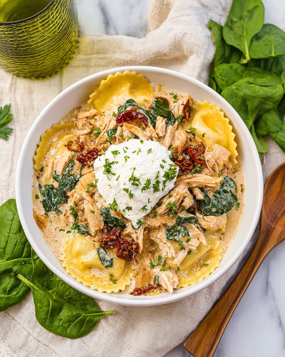 A white shallow bowl holds a layered pasta dish with wide yellow ravioli at the base, topped with shredded light brown chicken and scattered pieces of sun-dried red tomatoes. Bright green chopped herbs are sprinkled over the top, along with a dollop of white ricotta cheese placed slightly off-center. The dish sits on a white cloth, with fresh green spinach leaves nearby, and green glassware blurred in the white marbled textured background. photo taken with an iphone --ar 4:5 --v 7